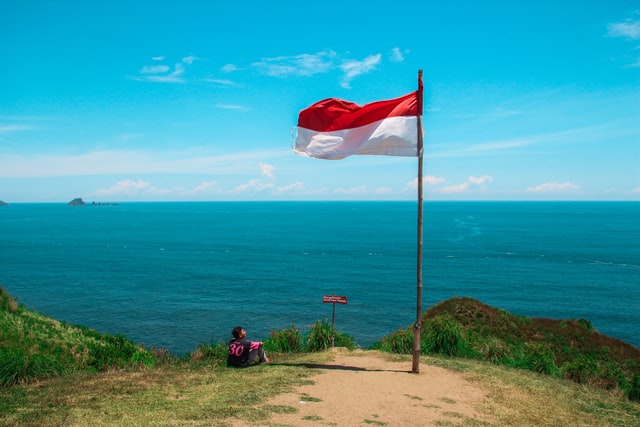 Bendera merah putih berkibar di tebing di atas pantai. UNSPLASH/Anggit Rizkianto